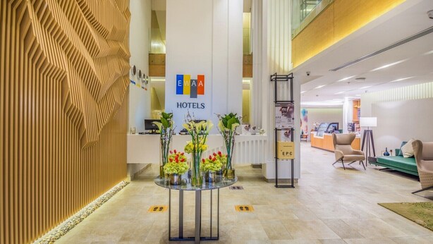 A hotel reception area with a modern design, featuring a reception desk, a glass partition, and a seating area with chairs and a sofa. - Ewaa Express Hotel - AlRawda (Jeddah)