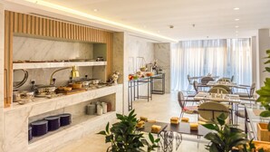 A modern dining area with marble countertops, a buffet setup, and a seating arrangement with tables and chairs. - Ewaa Express Hotel - AlRawda (Jeddah)