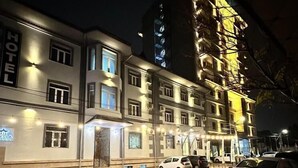 A multi-story hotel with illuminated signage, a wet street, and parked cars. - Stella Hotel (Tashkent)