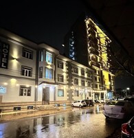 Un hotel de varios pisos con señalización iluminada, una calle mojada y coches estacionados.