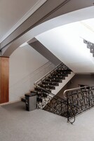 Una escalera con barandillas negras ornamentadas, un pilar de madera y un bote de basura.