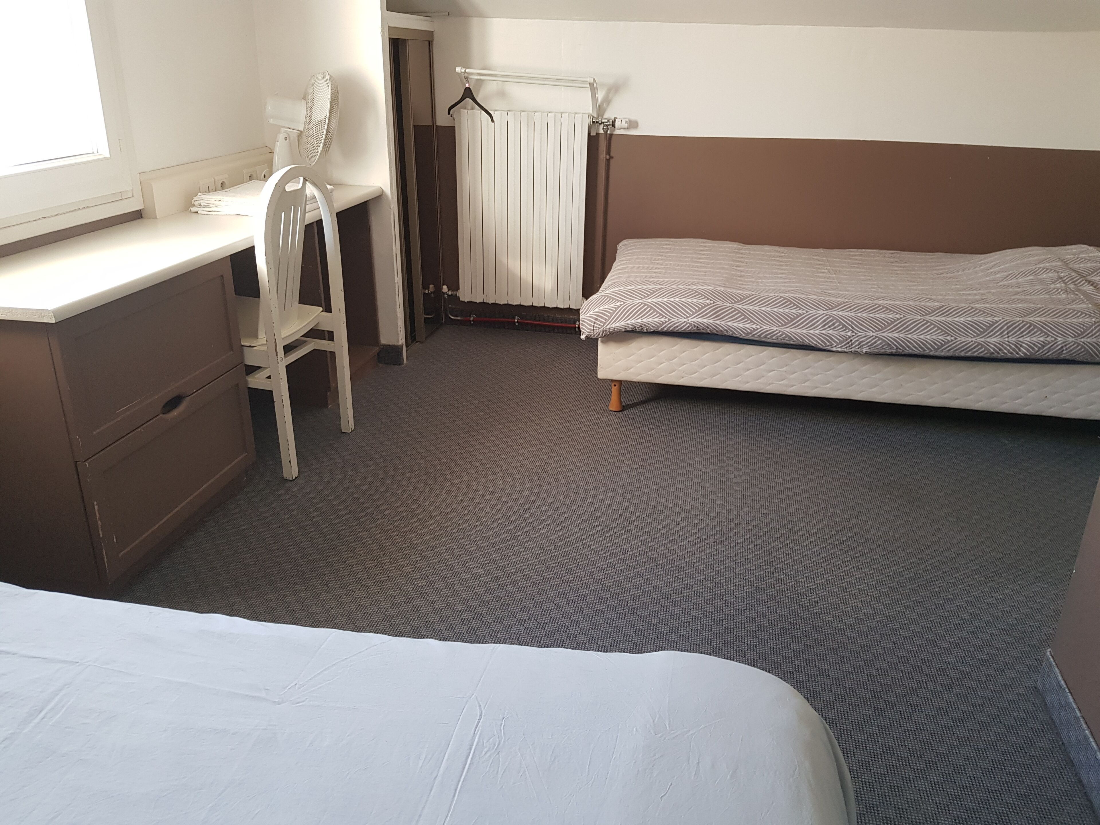 A bedroom with a single bed, a desk with a chair, a radiator, and a window.