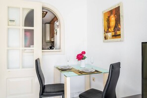 A dining area with a glass table, black chairs, a vase with flowers, and a painting on the wall.