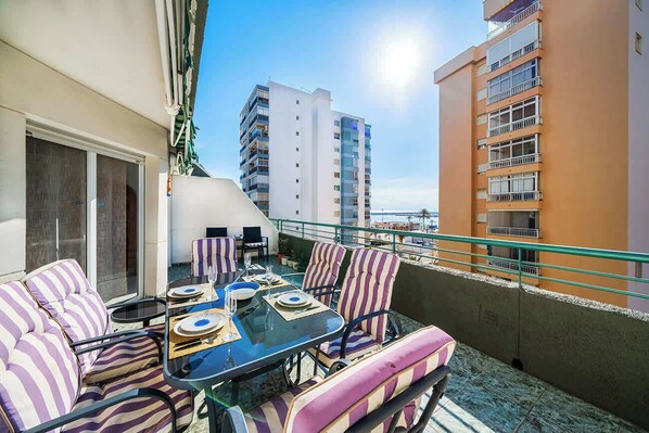 A balcony with a glass table, striped chairs, and a view of a tall building.