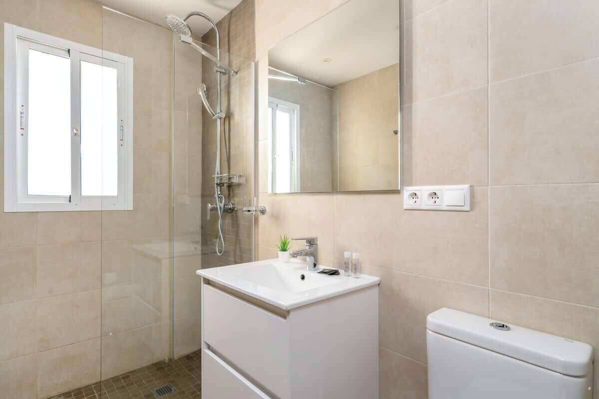 Ein modernes Badezimmer mit einer gläsernen Duschkabine, einem weißen Waschbecken mit Spiegel darüber und einer Toilette.