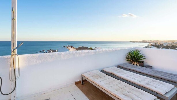 Un balcó amb vista al mar, una dutxa i dues zones d'seients amb coixins.