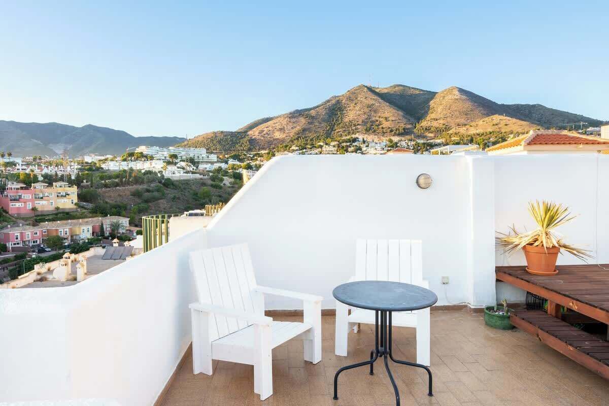 Eine Dachterrasse mit weißen Stühlen und einem Tisch, mit Blick auf eine Stadtlandschaft und Berge.