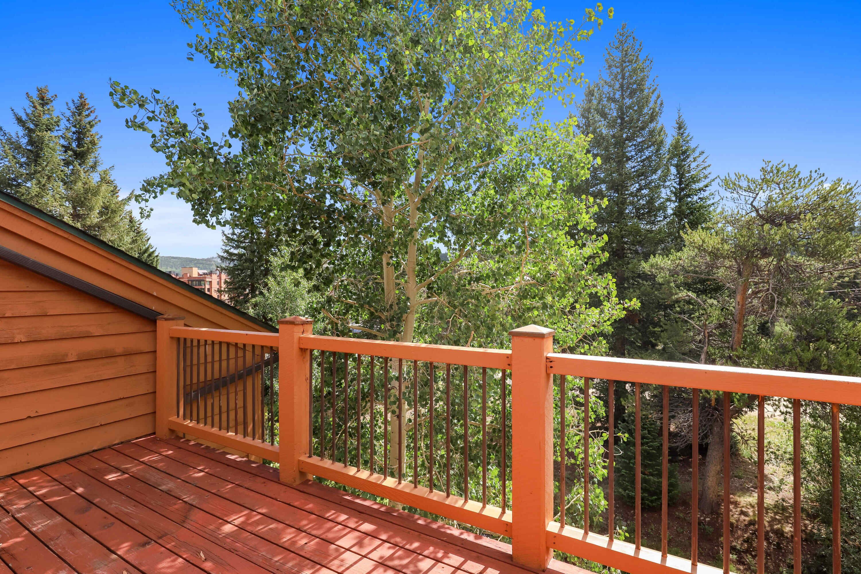 A wooden deck with a railing, surrounded by trees and a clear sky.