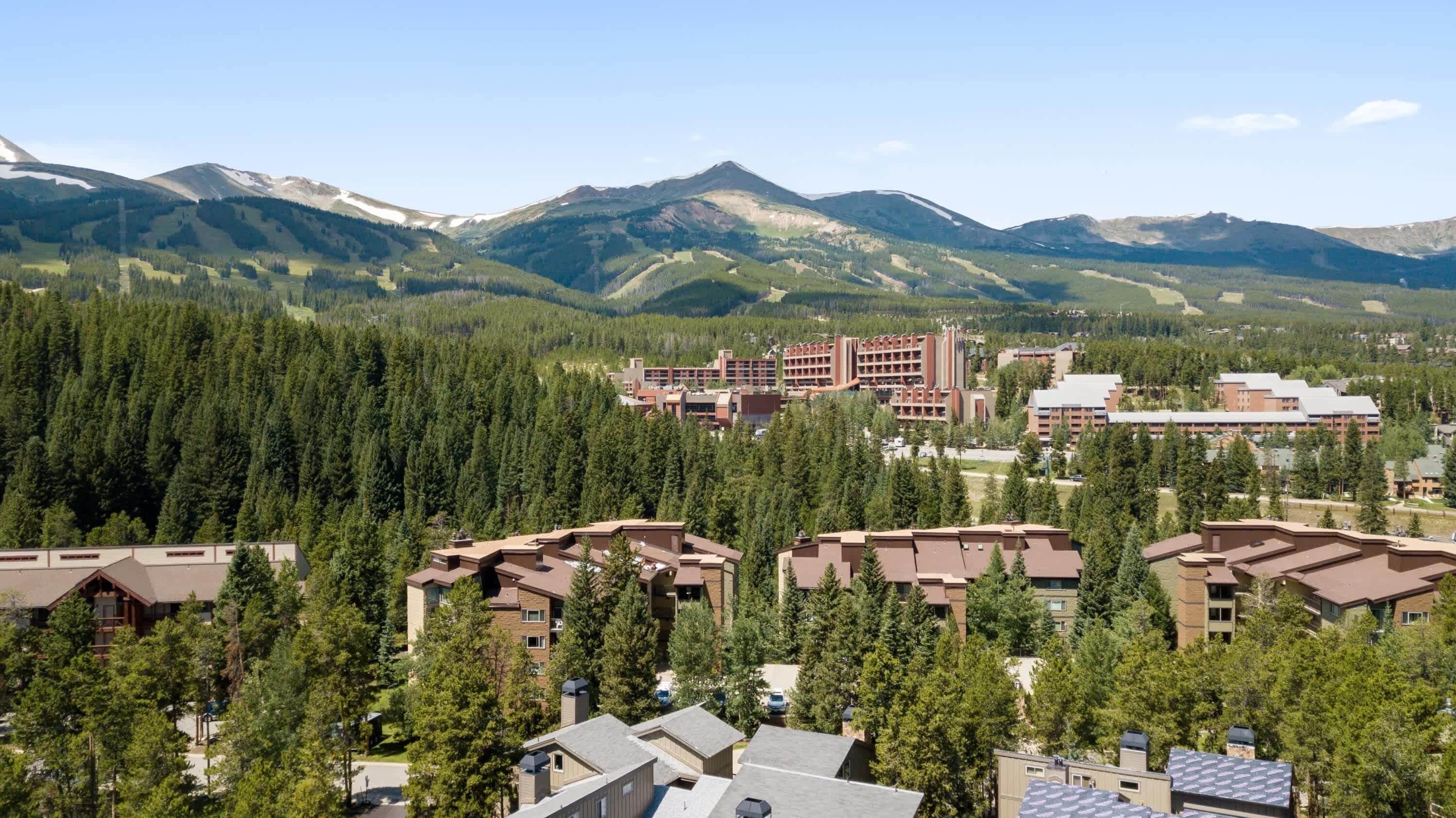 A mountain resort with multiple buildings surrounded by dense forests and snow-capped peaks.