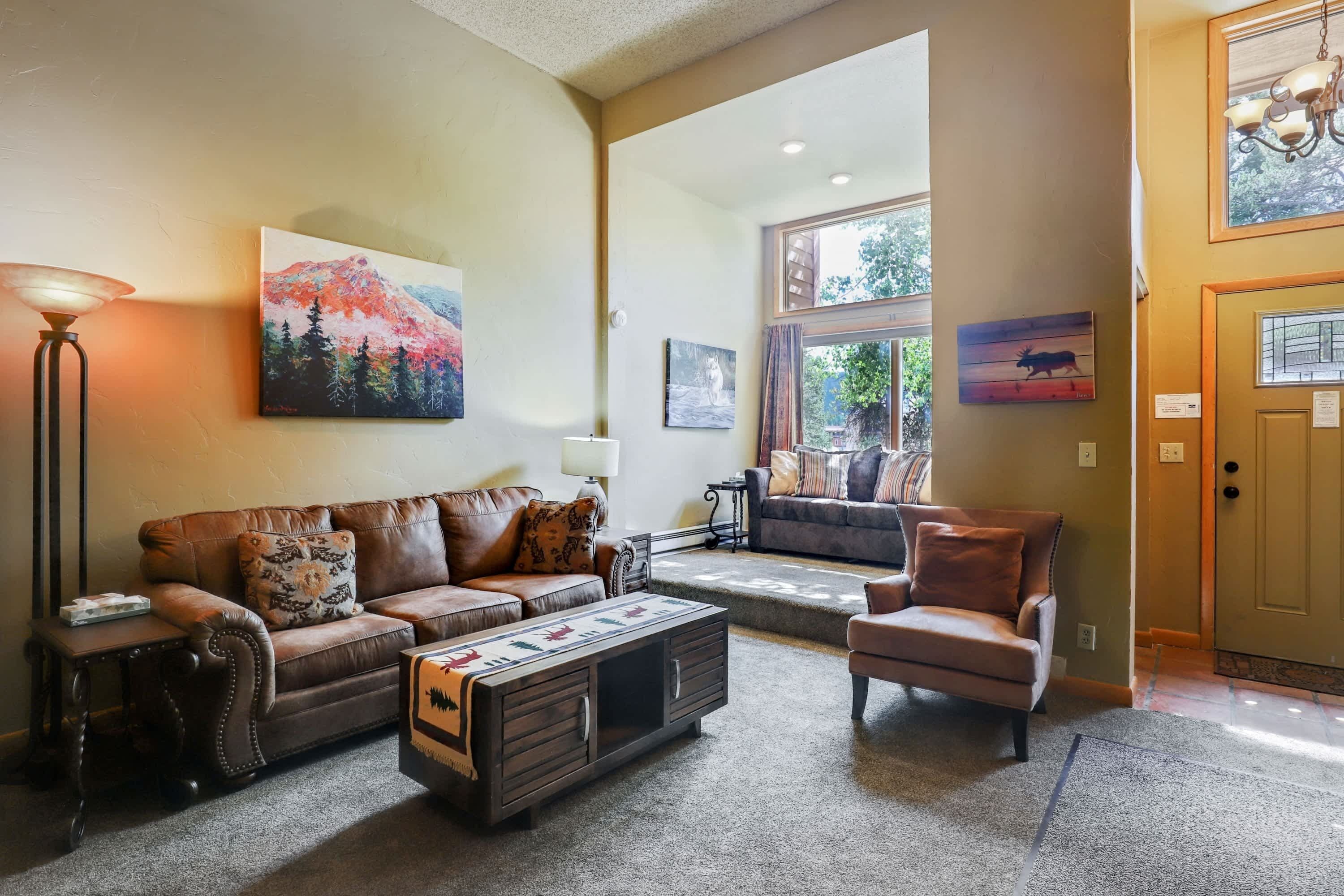 A living room with a brown leather sofa, a wooden coffee table, and a brown armchair. There is a painting of a mountain on the wall and another painting of a buffalo on the adjacent wall.