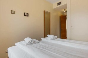 A hotel room with two beds, each with neatly folded towels, a large mirror, and a wooden door. - Poolfront garden apt by Costarentals - Ref 46 (La Cala de Mijas)