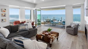 A spacious living room with a large sofa, a coffee table, and a view of the ocean through large windows. - UPPER LEVEL Pet Friendly Oceanfront Condo P923-0 (Oceanside)