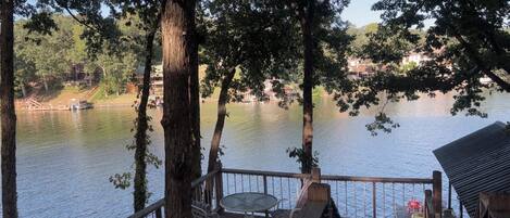A wooden deck with a table and chairs overlooking a calm lake, surrounded by trees.