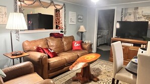 Un soggiorno con un divano in pelle marrone, un tavolino in legno, un tappeto decorato, una televisione e una zona pranzo con tavolo e sedie.
