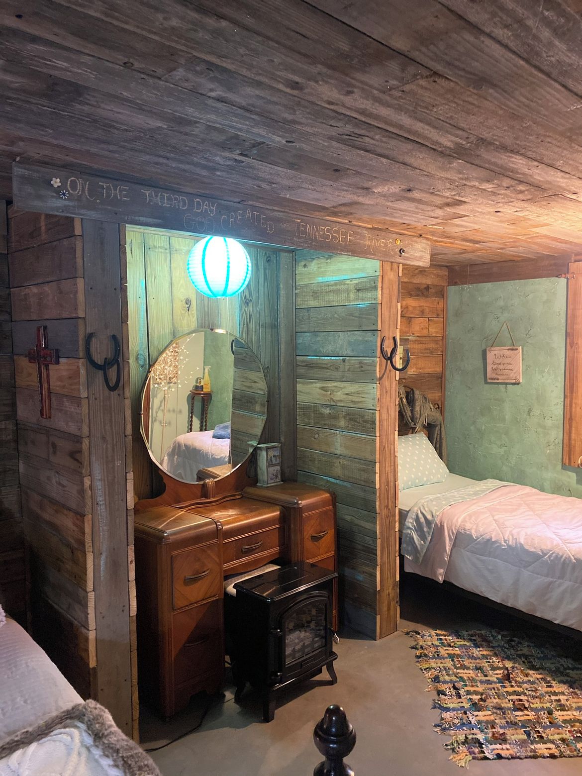 Una habitación rústica con techo de madera, una cama, un tocador con espejo y una alfombra pequeña.