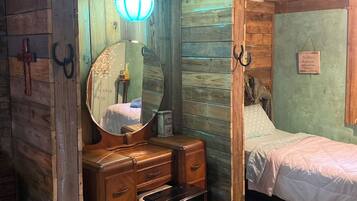 Una habitación rústica con techo de madera, una cama, un tocador con espejo y una alfombra pequeña.