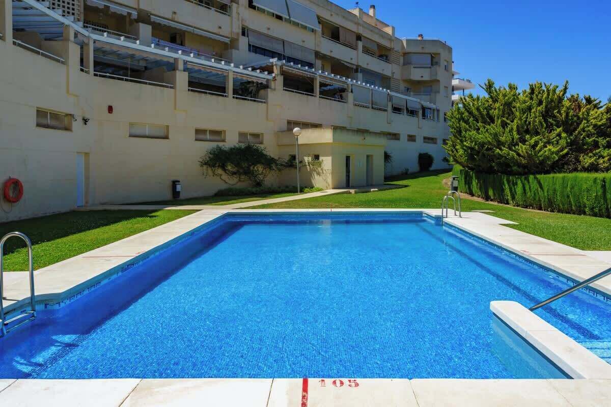 Une piscine à l’eau d’un bleu limpide, entourée d’une pelouse bien entretenue et d’un immeuble à plusieurs étages doté de balcons.