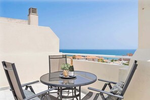 A round table with chairs on a balcony overlooking the sea.
