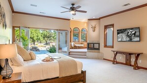 A bedroom with a bed, a nightstand, a desk, a ceiling fan, and a large window.