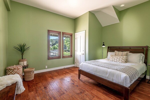 Un dormitorio con cama de madera, paredes verdes, dos ventanas, una puerta y una planta en maceta.