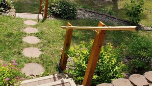 Una escalera de madera que conduce a un muelle junto a un lago, rodeado de follaje y un sendero de piedra.