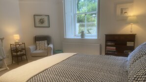 Une chambre à coucher avec un lit, une chaise, une bibliothèque, une fenêtre et un radiateur.
