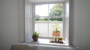 Une pièce avec une grande fenêtre, un radiateur, une plante en pot et une petite table sur laquelle se trouvent une balance et un bol.