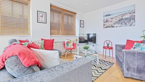 Una sala de estar moderna con un sofá gris, almohadas rojas, una mesa de centro de vidrio y un televisor.