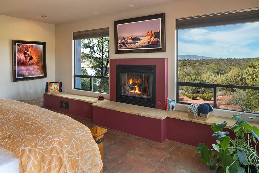 A bedroom with a fireplace, large windows, and a view of a mountainous landscape.