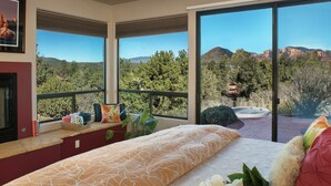 A bedroom with a large bed, a fireplace, and a view of a hot tub and mountains. - Walls of Glass - Panoramic Views, Hot Tub, Fire Pit Under the Stars (Sedona)