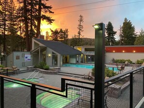 A pool area with a small building, a fenced deck, and a sunset in the background.