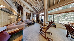 A spacious living room with a stone fireplace, large windows, and a wooden ceiling. - Comfortable 4 Bdrm Condo with Easy Access to Mammoth Mountain, lifts, and the Village Gondola (Unit 632 at 1849) by RedAwning (Mammoth Lakes)