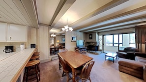 A spacious living area with a wooden dining table, comfortable seating, a fireplace, and a large window providing natural light.