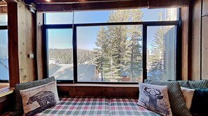 Cozy cabin with a forest view, featuring a plaid-patterned bench and a large window.