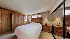 A bedroom with a large bed, wooden wardrobe, two bedside tables with lamps, and a large mirror.