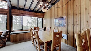 A wooden interior with a large dining table, chairs, and a chandelier.