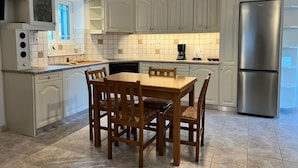 A kitchen with white cabinets, a stainless steel refrigerator, a wooden dining table with chairs, and a tiled backsplash.