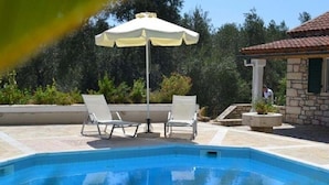 A swimming pool with two lounge chairs and an umbrella, surrounded by stone buildings and greenery.