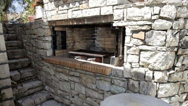 A stone-built outdoor kitchen with a built-in grill and a stone bench.