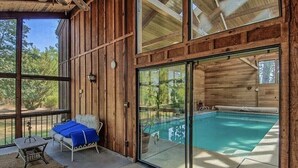 Una cabina di legno con piscina vetrata, un divano con cuscini blu e un tavolino.