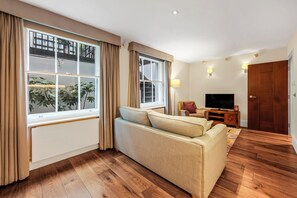 A living room with a sofa, a television, and a wooden floor. - Modern apartment with sofa bed, patio and private entrance (London)