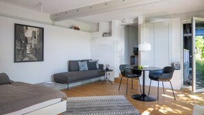 A modern room with a bed, a sofa, a dining table with chairs, a small side table, and a large window. - Modern Minimalistic Seeblick Design Studio mit Küche, Terrace und Parkplatz (Sipplingen)