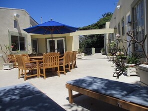 Eine Terrassengruppe mit Holztisch und -stühlen, einem blauen Sonnenschirm und einer Bank.