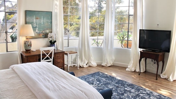 A bedroom with a large bed, a desk, a chair, a television, and a window with curtains. - Modern Home, Multi Unit, Relaxing Spacious Patio Ready for Fun! (Laguna Beach)