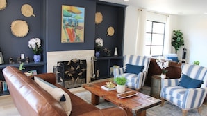 A living room with a brown leather sofa, striped armchairs, a wooden coffee table, and a fireplace. - Modern Home, Multi Unit, Relaxing Spacious Patio Ready for Fun! (Laguna Beach)