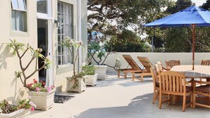An outdoor patio with a table and chairs, surrounded by potted plants and a blue umbrella. - Modern Home, Multi Unit, Relaxing Spacious Patio Ready for Fun! (Laguna Beach)
