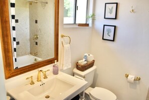 Ein Badezimmer mit einem weißen Waschbecken, goldenen Wasserhähnen, einem großen Spiegel, einer Toilette und gerahmten Bildern an der Wand.