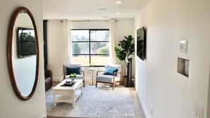 A modern living room with a large mirror, a sofa, a coffee table, and a window with curtains. - Modern Home, Multi Unit, Relaxing Spacious Patio Ready for Fun! (Laguna Beach)