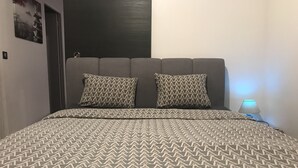 A bed with a patterned bedspread and two pillows, a bedside lamp, and a door in the background.