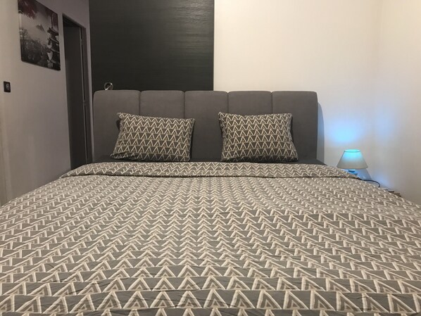 A bed with a patterned bedspread and two pillows, a bedside lamp, and a door in the background.